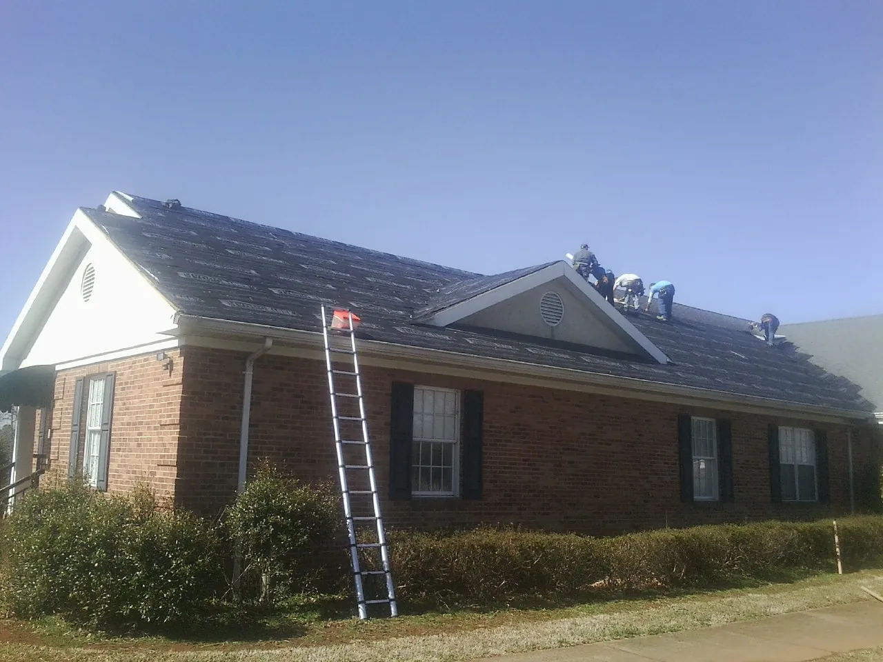 Crew tearing shingles off a brick ranch roof with a ladder set — Emergency Roof Repair work by our crew in Saint Francis