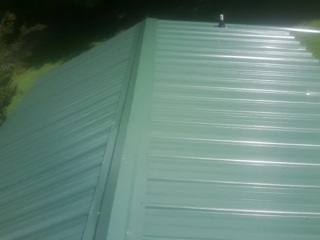 New green metal panels meeting at the ridge of a roof — Flat Roof Repair work by our crew in Saint Francis