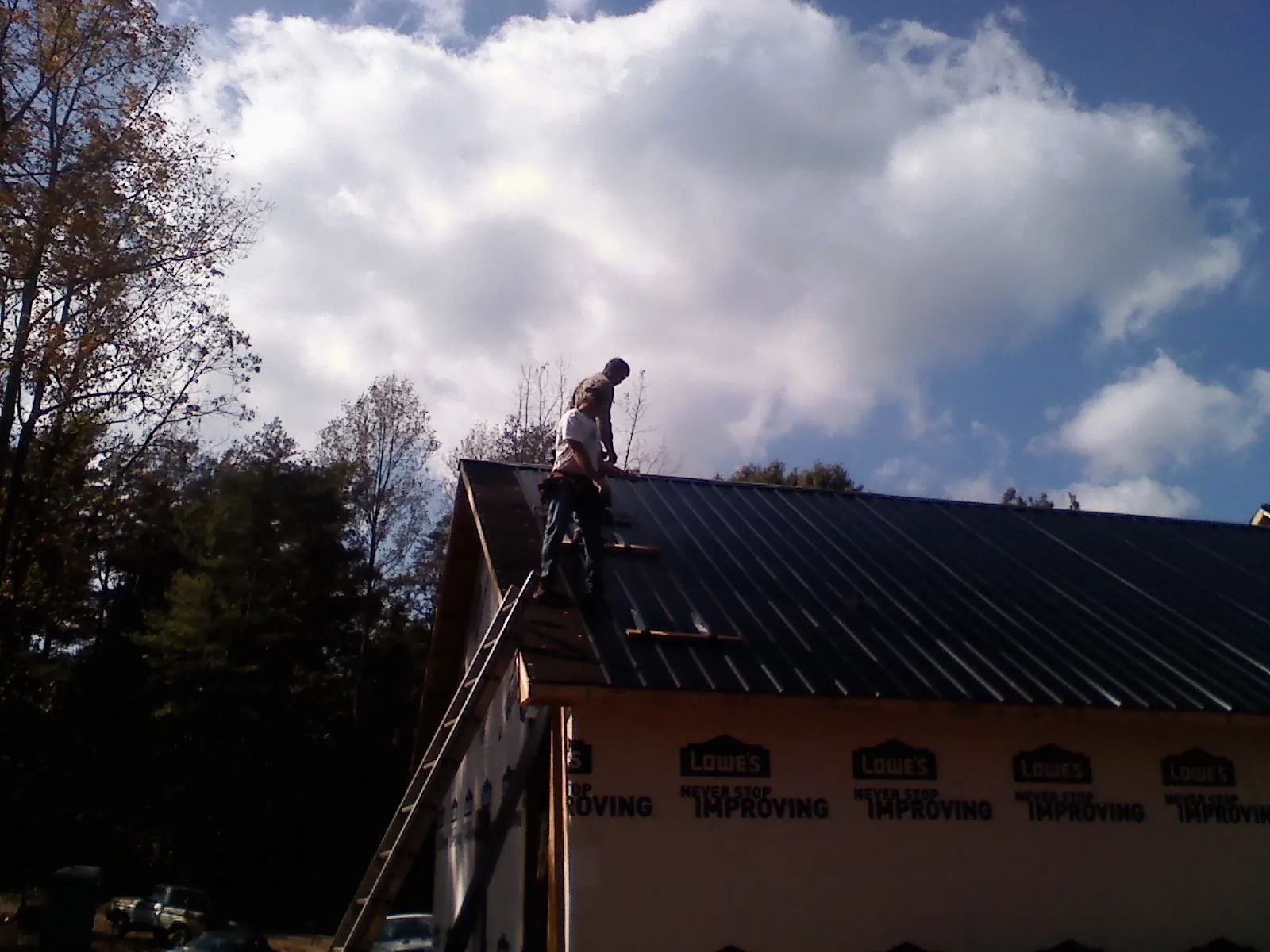 Roofer fastening dark metal panels high against a cloudy sky, from a Roof Inspection job in Saint Francis